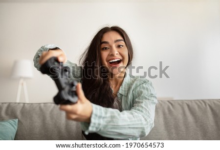 Cheerful Indian woman enjoying videogame on playstation, having fun indoors. Excited millennial gamer with joystick playing computer arcade. Stay home hobbies and activities Royalty-Free Stock Photo #1970654573