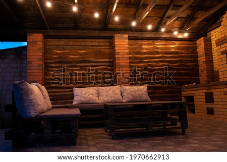 Barbecue area in the evening with antique light bulbs. Furniture made of wood and pallets.