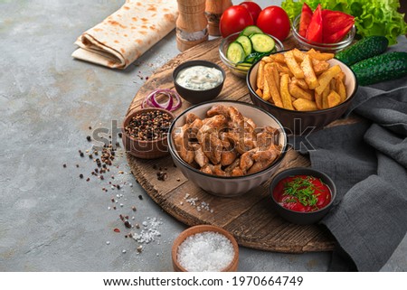 Grilled meat, French fries and vegetables on a gray background. Lunch, ingredients for making shawarma, burrito.