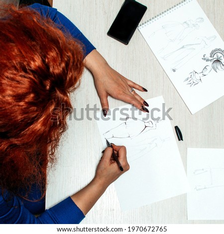 woman with red hair seamstress designer fashion draws sketches for her new dress lies mobile phone concept of small business, hobby at home production of clothes