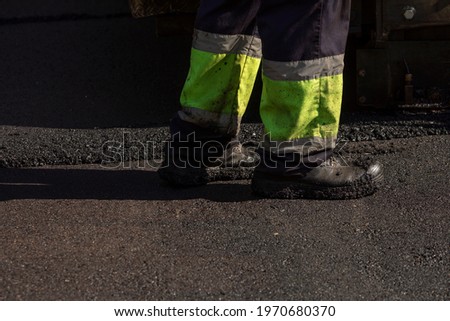 The boots of a worker, carrying out maintenance and asphalting of streets in Madrid, Retiro district, finishing the work of the asphalt paving machine and the rollers.