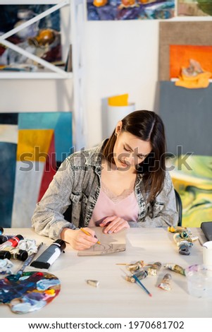 Painting hobby. Modern art. Home craft leisure. Inspired artist woman enjoying sketching with pencil at messy workplace in studio with colorful abstract artwork collection.