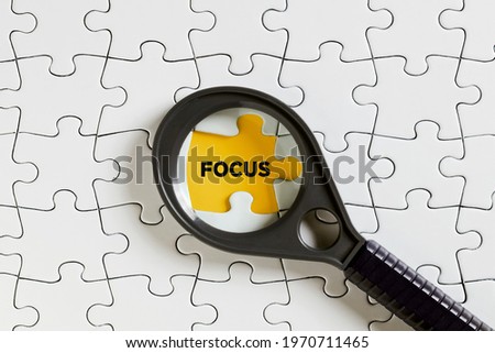 The word focus on missing puzzle piece with a magnifying glass. To focus or concentrate on a subject.