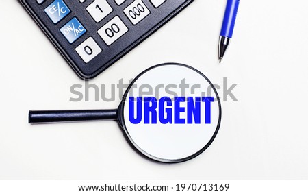 On a light background, a black calculator, a blue pen and a magnifying glass with text inside the word URGENT. View from above