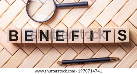 The word BENEFITS is written on wooden cubes on a wooden background next to a handle and a magnifying glass.