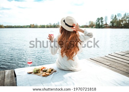 Young beautiful hipster woman in trendy summer sundress and hat. Carefree woman making picnic outside. Positive model sitting on blanket, eating fruits, drinking rose wine Royalty-Free Stock Photo #1970721818