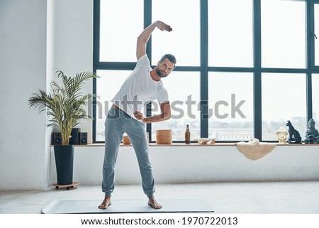 Full length of handsome young man doing fitness training at home while standing on the carpet
