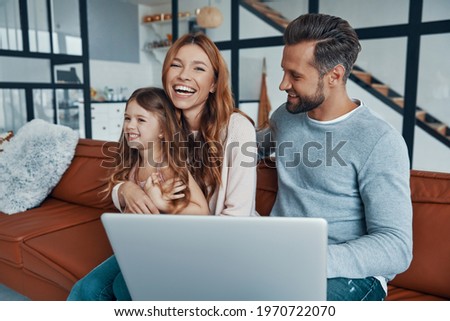 Playful beautiful family with little girl bonding together and smiling while using laptop at home