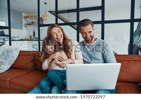 Playful beautiful family with little girl bonding together and smiling while using laptop at home