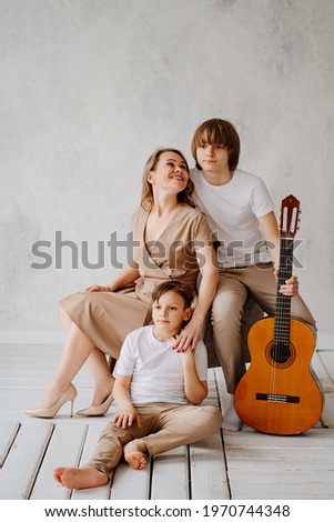 A mom and two sons in beige and white clothes pose for a photo shoot in the studio. happy single mother. memorabilia for the family. relationship between teenage children and parents. playing guitar