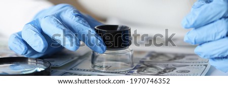 Woman in rubber gloves looking at dollar bills through magnifying glass