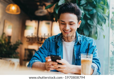 Young Asian man sitting and using smartphone at coffee shop Royalty-Free Stock Photo #1970808794