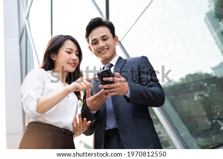 Two Asian business people using smartphone and talking together Royalty-Free Stock Photo #1970812550