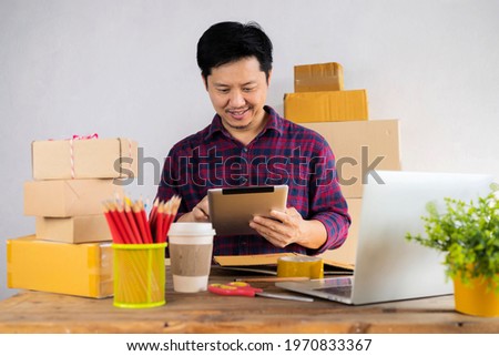 Businessman use tablet thinking with pile of parcel on work desk. Laptop at workplace of start up, small business owner. cardboard parcel box of product for deliver to customer. Online selling concept