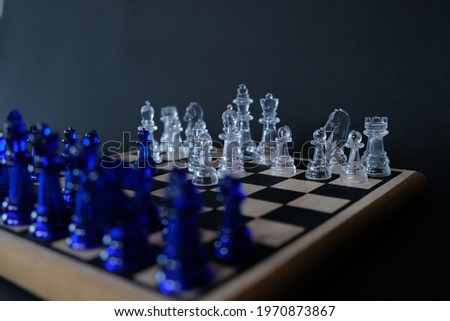 Two chess teams one in front of other on the chessboard. Blue and transparent chess team on black background.