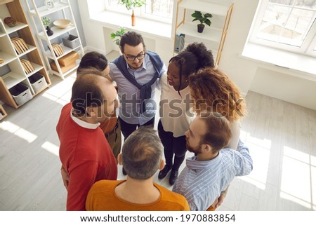 High angle group shot of mixed race people huddling in office. View from above of team of happy diverse business partners standing in circle embracing each other. Teamwork, support and unity concepts