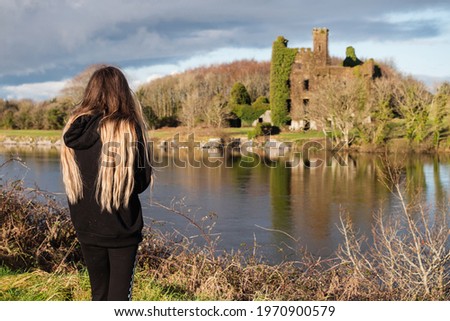 Young teenager girl looking at Menlo castle. Galway city, Ireland, River Corrib. The model dressed in black, has long blond and black hair.