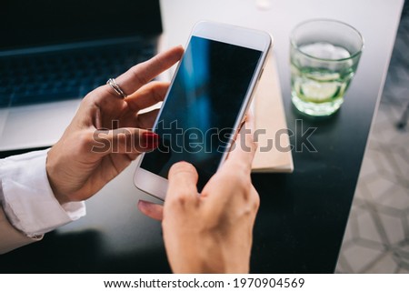 Cropped image of female holding mobile phone with empty screen sending and texting messages in chatting application, woman's hands typing publication for share in blog via smartphone and 4G