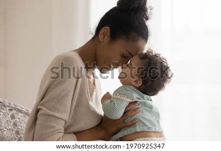 Happy young African American mom hug cuddle with little baby kid daughter at home. Smiling mixed race ethnicity mother embrace small ethnic newborn toddler child show love care. Motherhood concept. Royalty-Free Stock Photo #1970925347