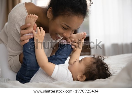 Overjoyed young African American mother relax play with smiling small biracial toddler daughter. Happy loving ethnic mom have fun enjoy motherhood with little baby girl child. Parenthood concept. Royalty-Free Stock Photo #1970925434