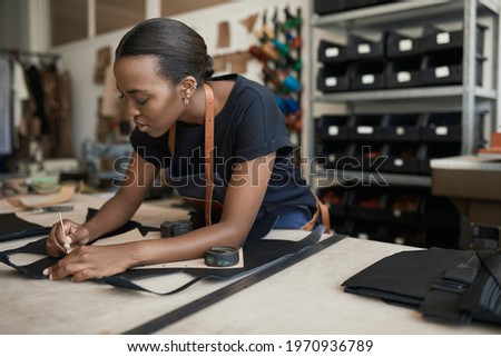 African female artisan using a pattern on leather in her shop Royalty-Free Stock Photo #1970936789