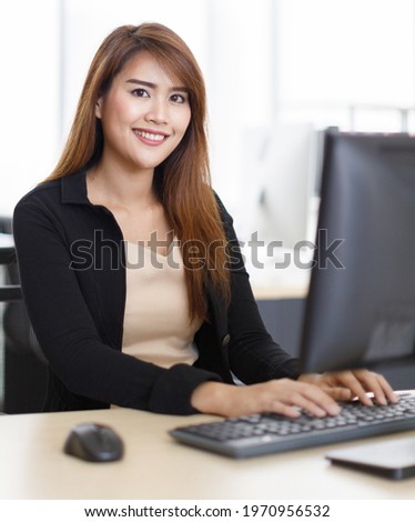 Asian young smart successful female assistant employee in formal dress sitting smiling look at camera working typing business information by keyboard at computer desk with mouse in company office.