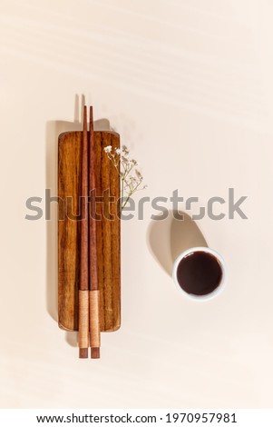 Romantic oriental style composition with wooden chopsticks and soy sauce in a white porcelain sauce pan on a pink background with copy space. Eco friendly accessories for food. Food mockup. Top view