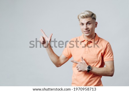 Blonde man in pointing away at copy space with two fingers isolated over gray background