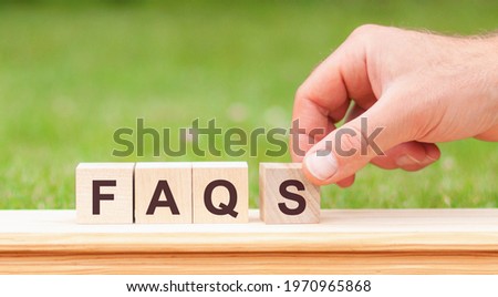 Word faqs written with wooden blocks. Man hand holding wooden cube block with warning - business word on green lawn background. faqs - short for Frequently Asked Questions