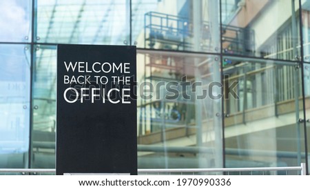Welcome back to the office on a city-center sign in front of a modern office building	