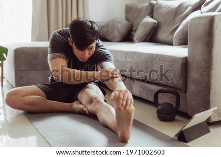 Fit man in sportwear streching after exercise at home. Young asian man streching before workout. Royalty-Free Stock Photo #1971002603