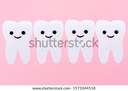 A row of white teeth with cartoon smiling faces, carved out of felt. Pink background. Copy space. The concept of stomatology and oral hygiene.
