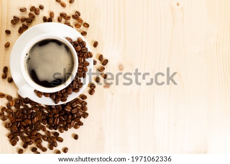 Cup of black coffee with coffee beans on wooden table. Top view with copy space.