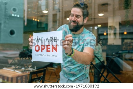 Happy man placing opening poster after coronavirus on the glass of his business
