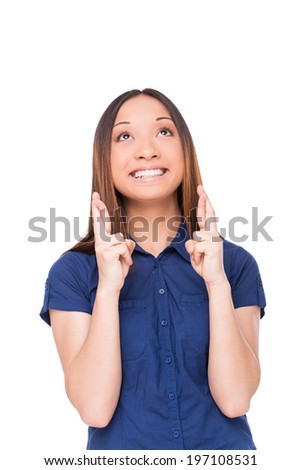 Waiting for special moment. Cheerful young woman looking up and keeping fingers crossed while standing isolated on white