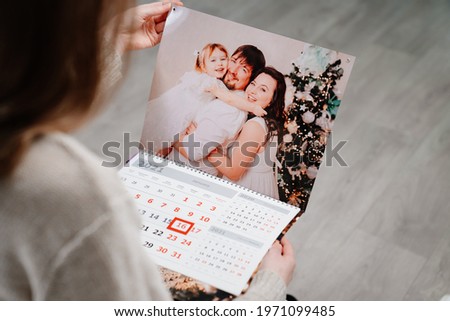 A woman looks at a calendar with a family photo. A useful gift with your photos. Souvenir. additional photographer's service. Royalty-Free Stock Photo #1971099485