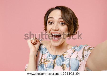 Close up young happy woman with short hairdo in trendy blouse do selfie shot on mobile phone do winner gesture clench fist isolated on pastel pink background studio portrait People lifestyle concept