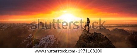Magical Fantasy Adventure Composite of Man Hiking on top of a rocky mountain peak. Background Landscape from British Columbia, Canada. Sunrise Dramatic Colorful Sky Royalty-Free Stock Photo #1971108200