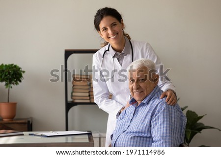My health is in safe hands. Happy young latin woman gp hug shoulders of old man visitor glad to help him feel well. Smiling doc and retired patient look at camera posing for portrait in doctor office Royalty-Free Stock Photo #1971114986