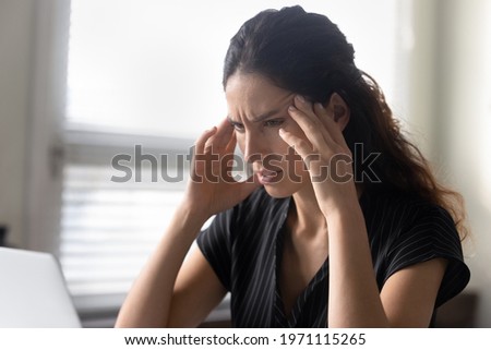 What should I do. Stressed latina woman sit by pc rub temples feel information overload unable to focus attention on work. Anxious young female try to remember important thing solve unexpected problem Royalty-Free Stock Photo #1971115265