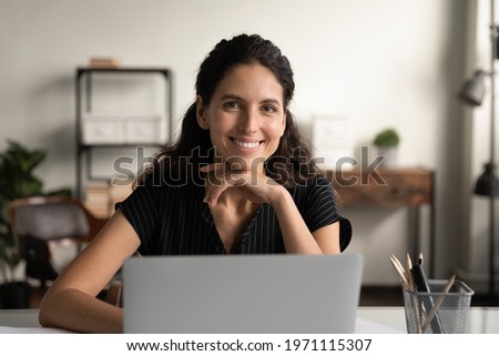 Happy worker. Headshot portrait of confident young latin female posing by office computer at work desk. Smiling successful millennial woman remote employee freelancer sit at workplace look at camera