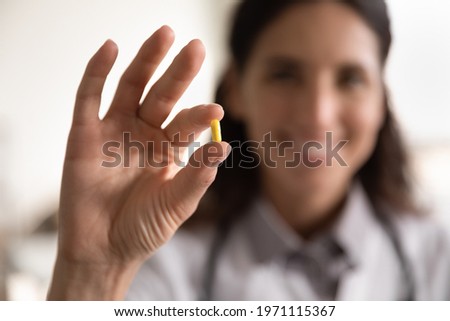 Pharmacological therapy. Close up portrait of smiling female doctor scientist pharmacist looking at camera presenting new effective pill medicine. Focus on yellow capsule in woman medical worker hand Royalty-Free Stock Photo #1971115367