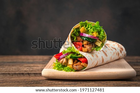 Chicken meat, French fries, vegetables and salad are wrapped in pita bread on a brown background. Traditional shawarma. Side view, copy space. Royalty-Free Stock Photo #1971127481