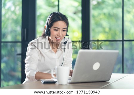 Asian Telemarketing or call center with headset working on computer lap top at home. Attractive Telesales talk and support remote customer. Operator service occupation business representative concept. Royalty-Free Stock Photo #1971130949