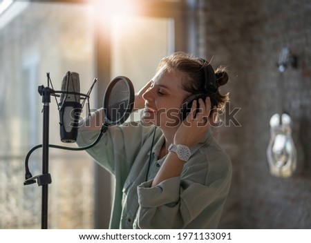 Young beautiful woman recording song singing into microphone, vocal lessons and recording industry
