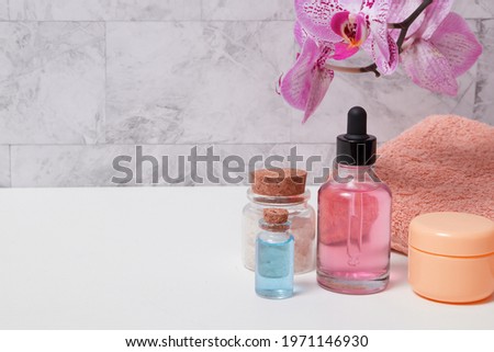 Bottles of tincture, salt, oil or serum, a towel and a blooming orchid over the towel in the bathroom. Skin care SPA concept