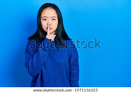 Young chinese girl wearing casual clothes asking to be quiet with finger on lips. silence and secret concept. 