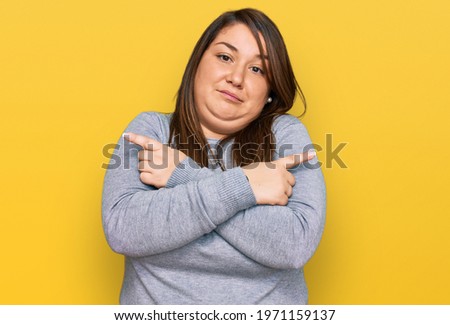 Beautiful brunette plus size woman wearing casual clothes pointing to both sides with fingers, different direction disagree 