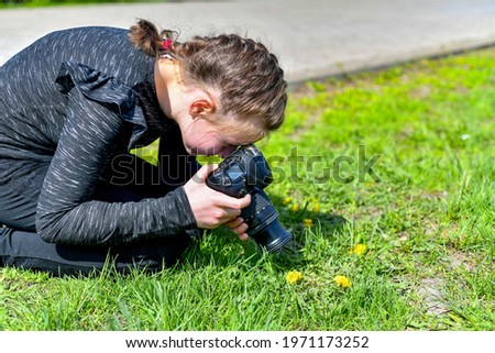 The girl takes a close-up photograph in the park on a SLR camera.