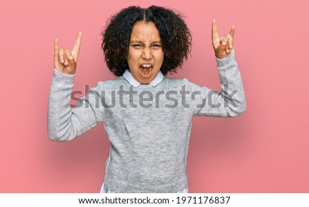 Young little girl with afro hair wearing casual clothes shouting with crazy expression doing rock symbol with hands up. music star. heavy concept. 